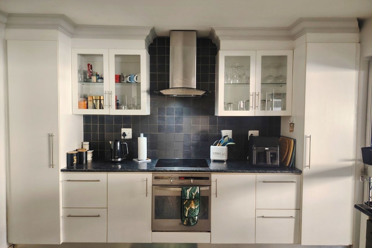 A well-maintained kitchen featuring white cabinetry, a dark tiled backsplash, integrated oven and hob, and stainless steel extractor fan.