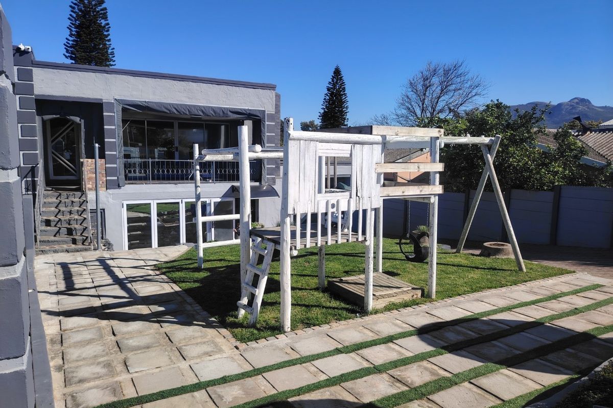 Rear exterior view featuring a paved patio area, a small lawn, and a multi-level house facade with sliding glass doors and an external staircase.