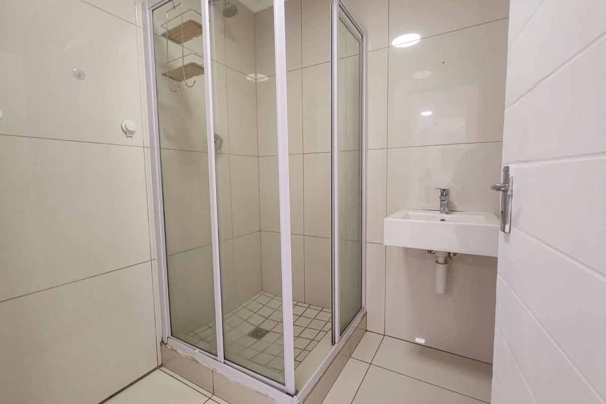 A clean, modern bathroom featuring a glass shower enclosure, wall-mounted basin with mixer tap, and neutral floor-to-ceiling wall tiles.