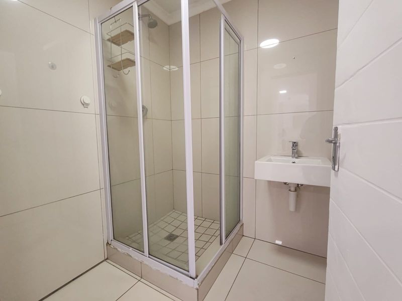 A clean, modern bathroom featuring a glass shower enclosure, wall-mounted basin with mixer tap, and neutral floor-to-ceiling wall tiles.