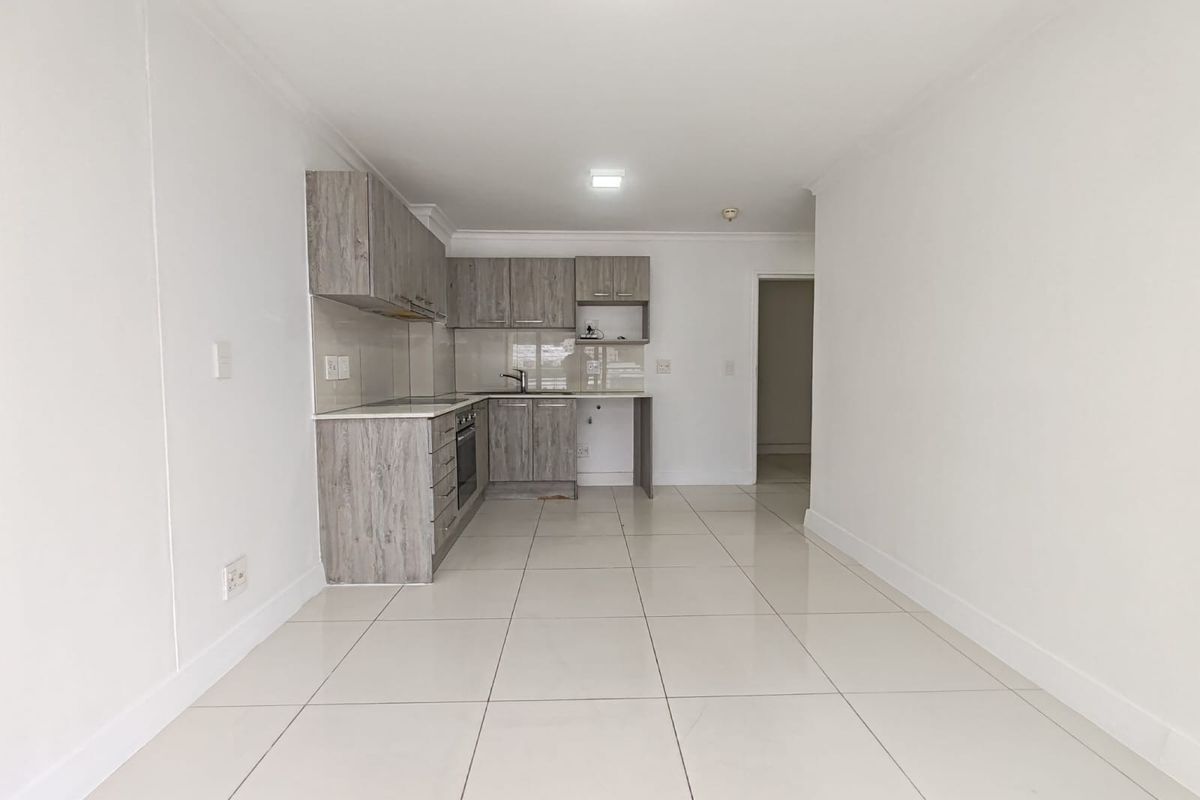 A clean, modern kitchen featuring light wood-grain cabinetry, tiled flooring, and integrated appliances, presented in an empty, well-maintained space.
