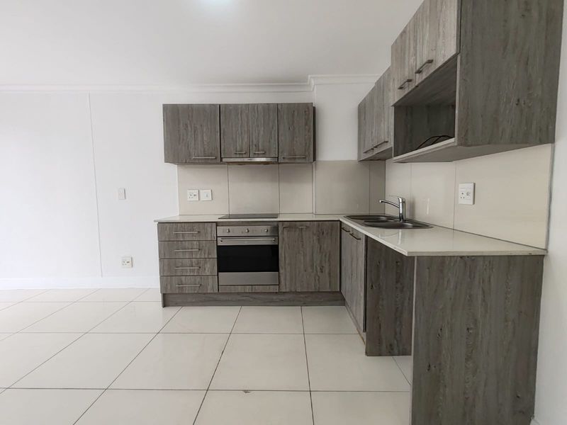 Modern kitchen featuring grey wood-grain cabinetry, stone countertops, built-in electric oven and hob, and neutral tiled flooring in an open-plan layout.