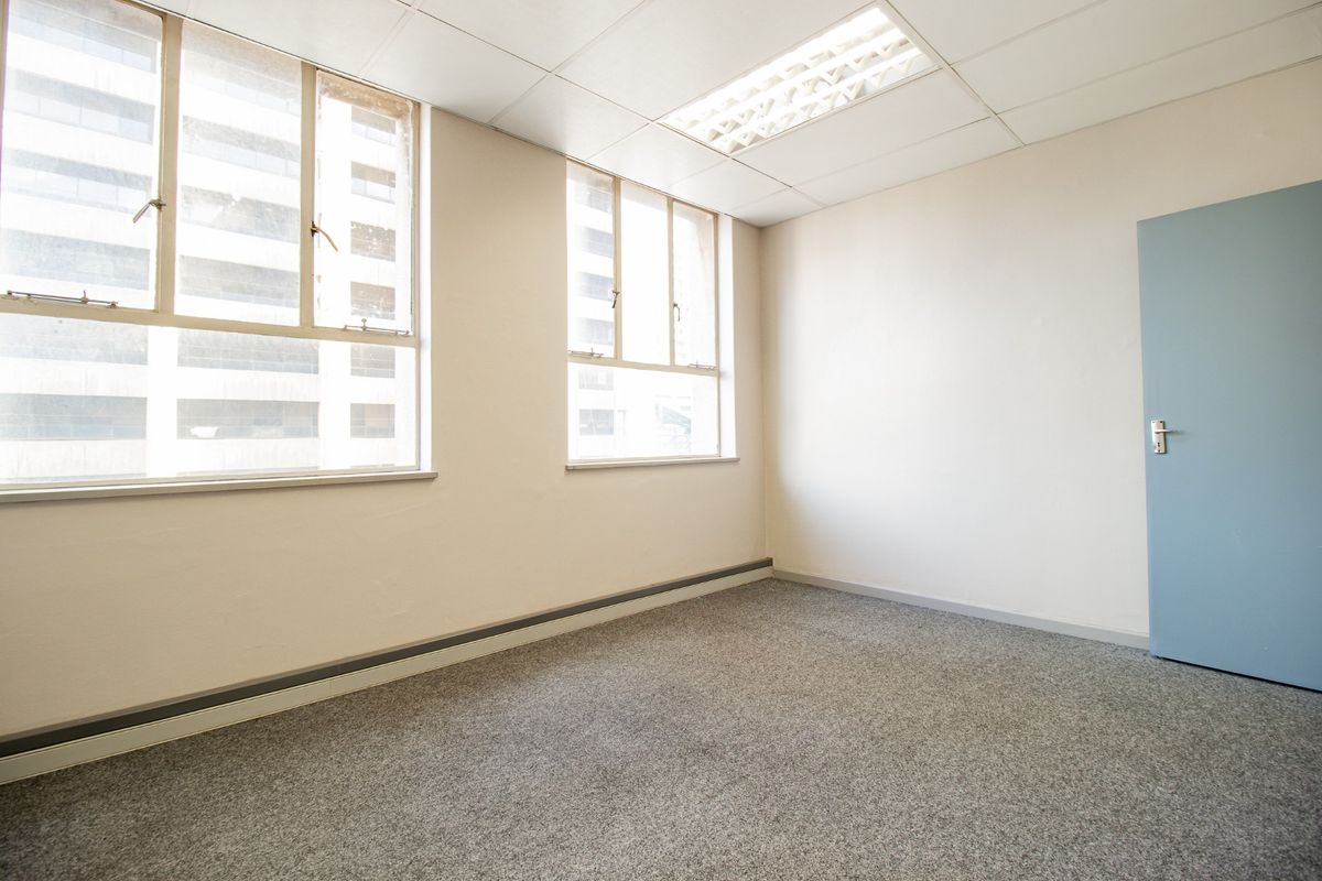 A vacant commercial office space featuring neutral walls, carpeted flooring, suspended ceiling with recessed lighting, and large windows providing natural light.