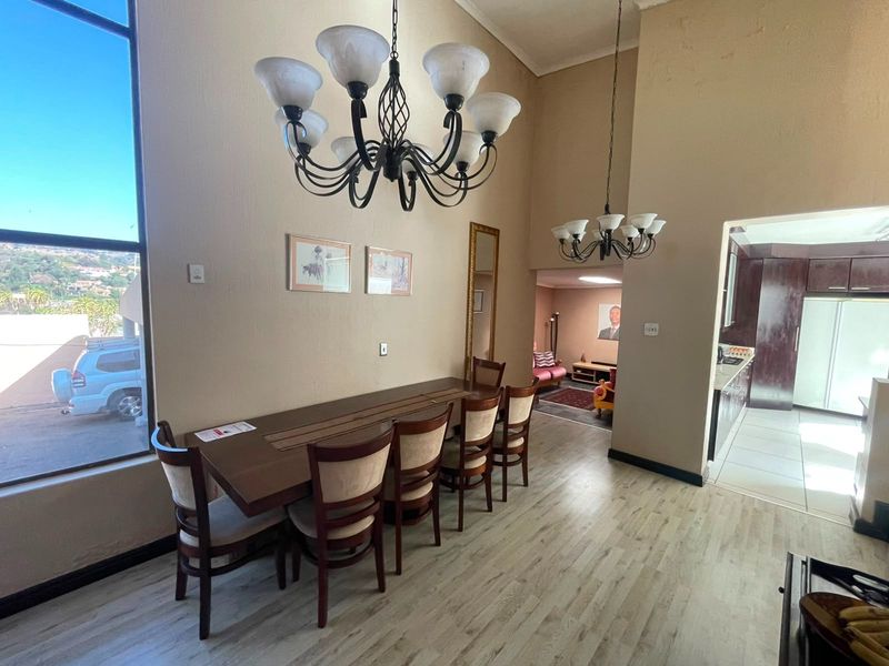 Dining area featuring high vaulted ceilings, large windows providing natural light, dual chandeliers, and modern laminate flooring, with an open flow to the kitchen.