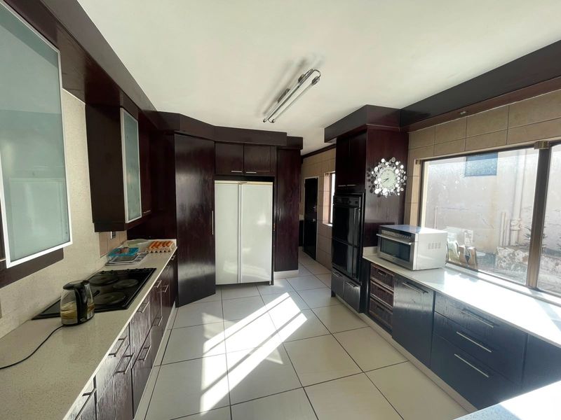 A functional kitchen featuring dark wood cabinetry, stone countertops, built-in double oven, and electric hob with tiled flooring and backsplash.
