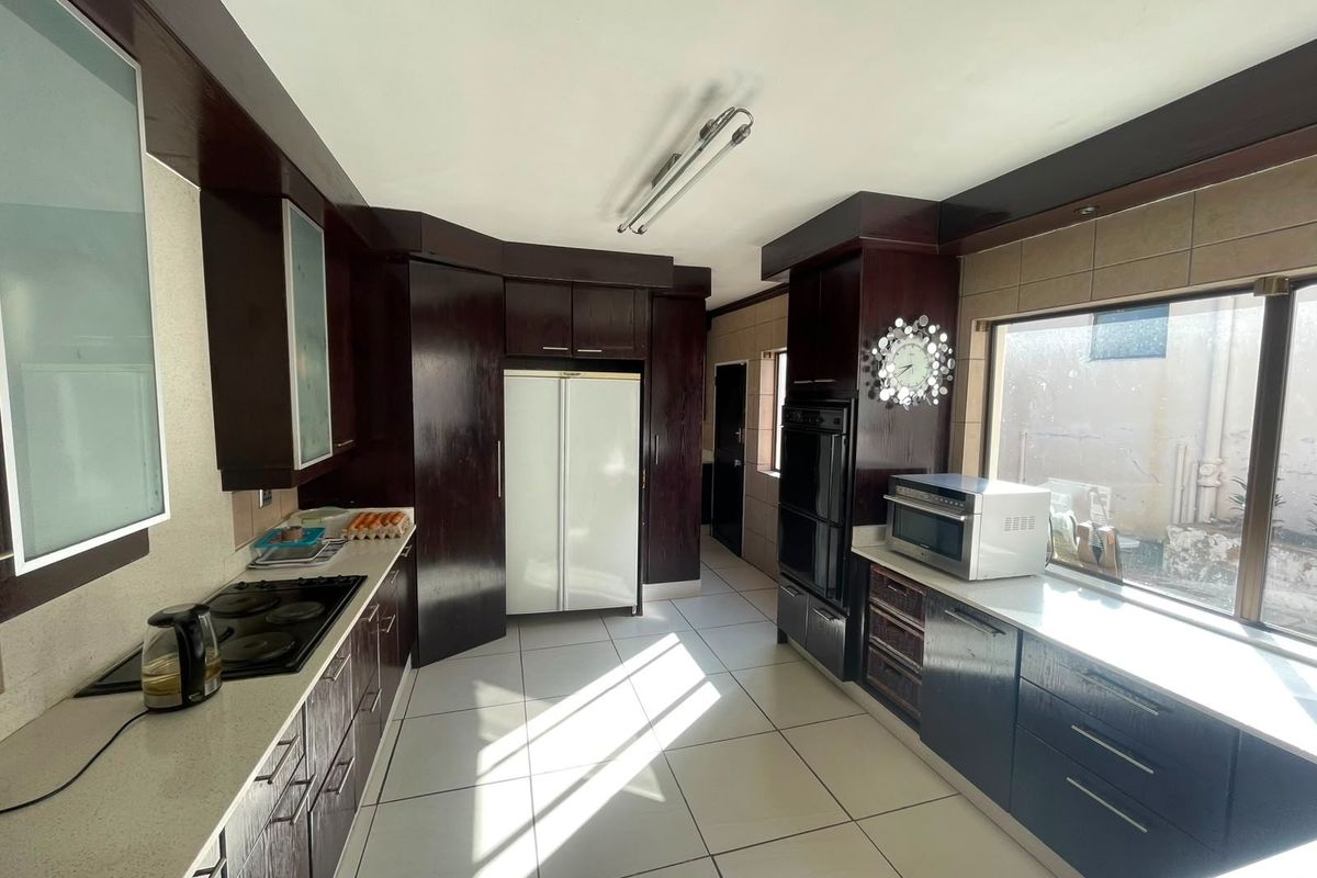 A functional kitchen featuring dark wood cabinetry, stone countertops, built-in double oven, and electric hob with tiled flooring and backsplash.