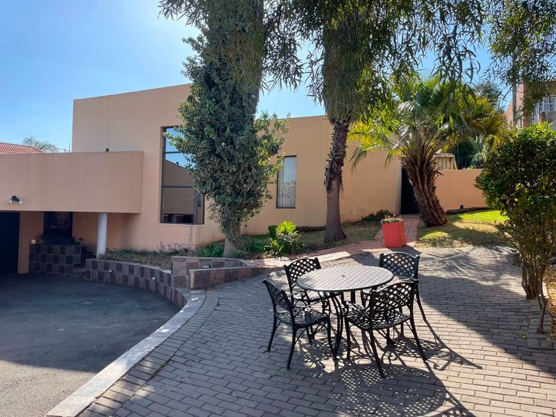 Rear exterior view featuring a paved patio area, landscaped garden, and access to the main dwelling with a retaining wall and tiled steps.