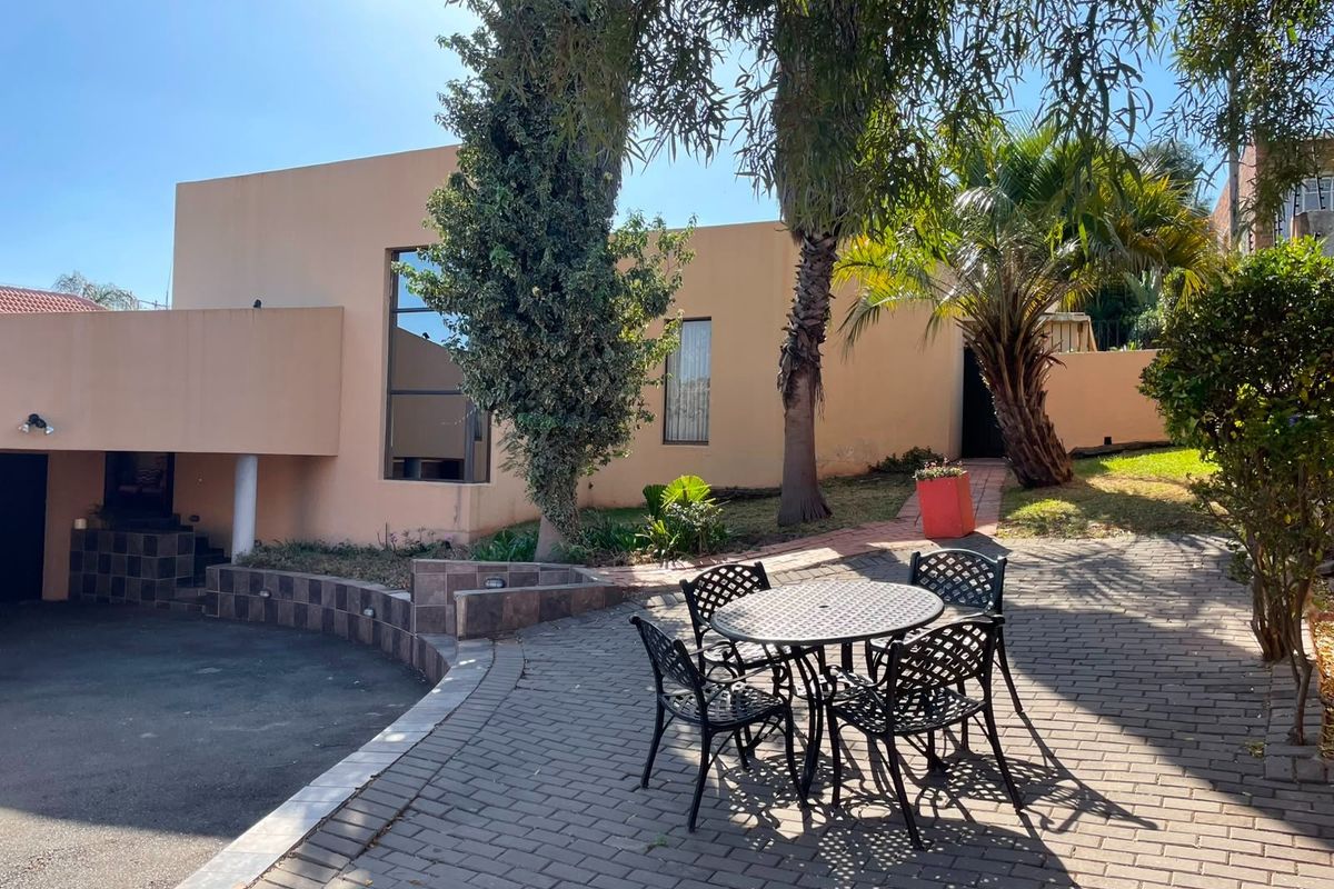 Rear exterior view featuring a paved patio area, landscaped garden, and access to the main dwelling with a retaining wall and tiled steps.