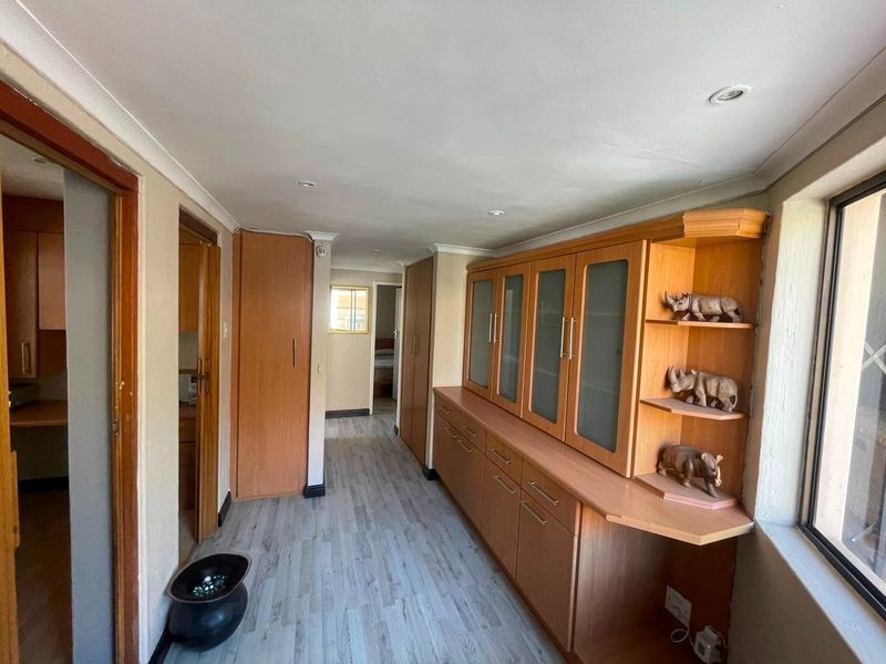 A functional hallway featuring extensive built-in wooden cabinetry, light-toned laminate flooring, and recessed ceiling lighting, providing ample storage space.