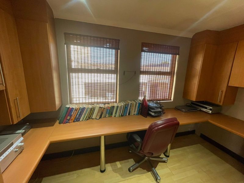 A functional home office featuring extensive built-in desk space and cabinetry, providing ample storage and workspace with natural light from dual windows.