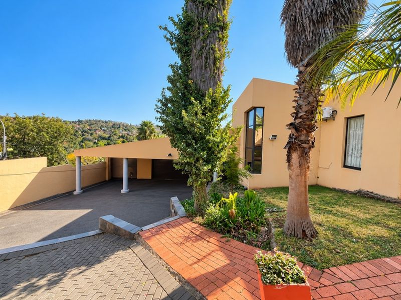 Front exterior view featuring a paved driveway, covered carport, brick walkway, and established garden area with mature palm trees.