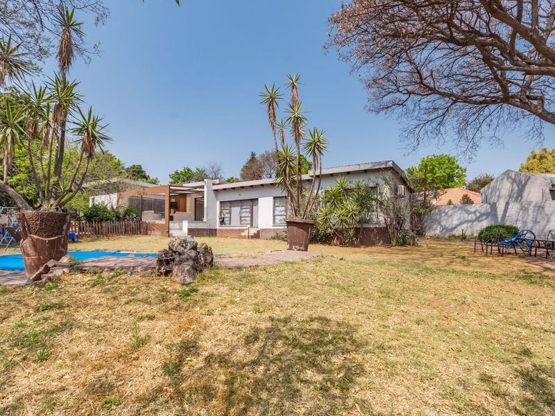 Rear view of the house featuring a swimming pool, covered patio, and a spacious garden area with established trees.