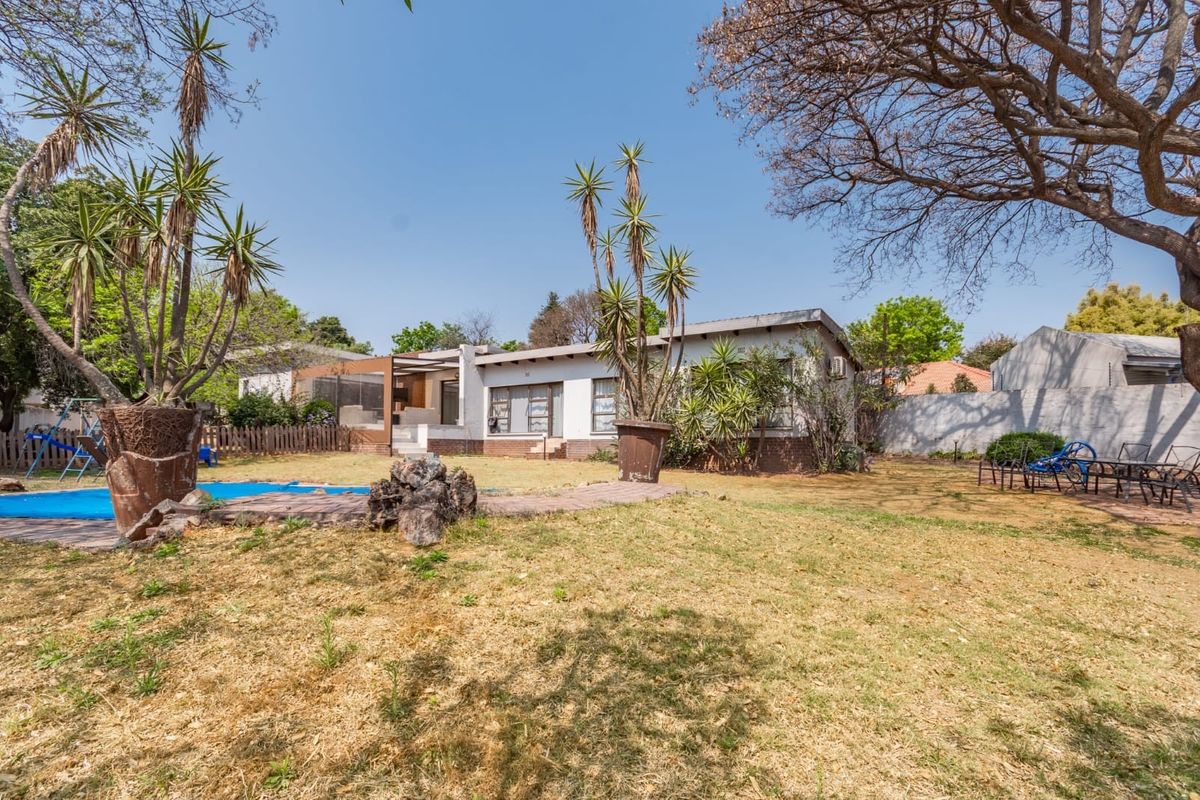 Rear view of the house featuring a swimming pool, covered patio, and a spacious garden area with established trees.
