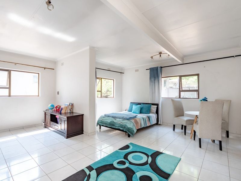 A spacious bedroom featuring tiled flooring, exposed ceiling beams, and multiple windows providing natural light.