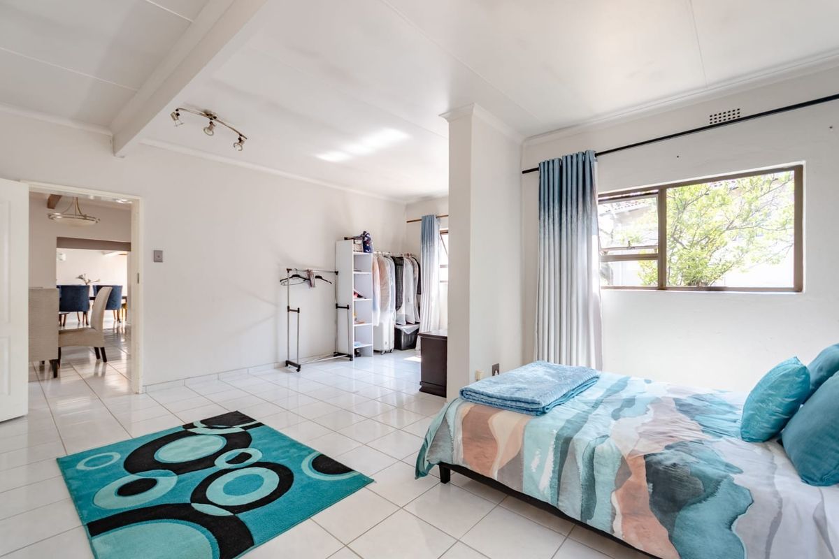 Spacious bedroom featuring white tiled flooring, neutral walls, and large windows allowing for natural light.