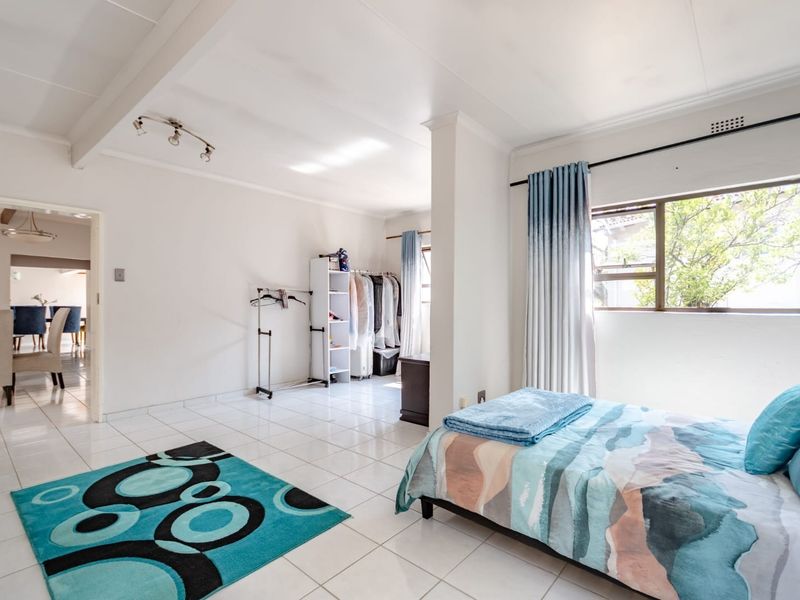Spacious bedroom featuring white tiled flooring, neutral walls, and large windows allowing for natural light.