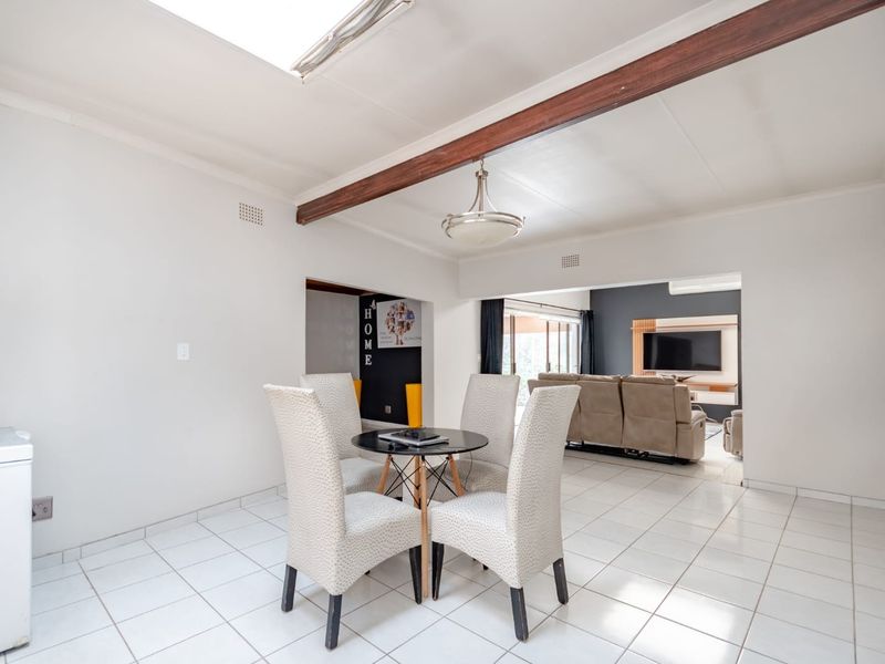 Open-plan living and dining area featuring tiled flooring, an exposed ceiling beam, and a skylight, creating a bright and connected living space.