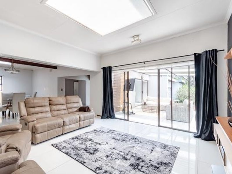 Spacious living room featuring large sliding glass doors leading to an outdoor patio, bright tiled flooring, and a central skylight for natural illumination.