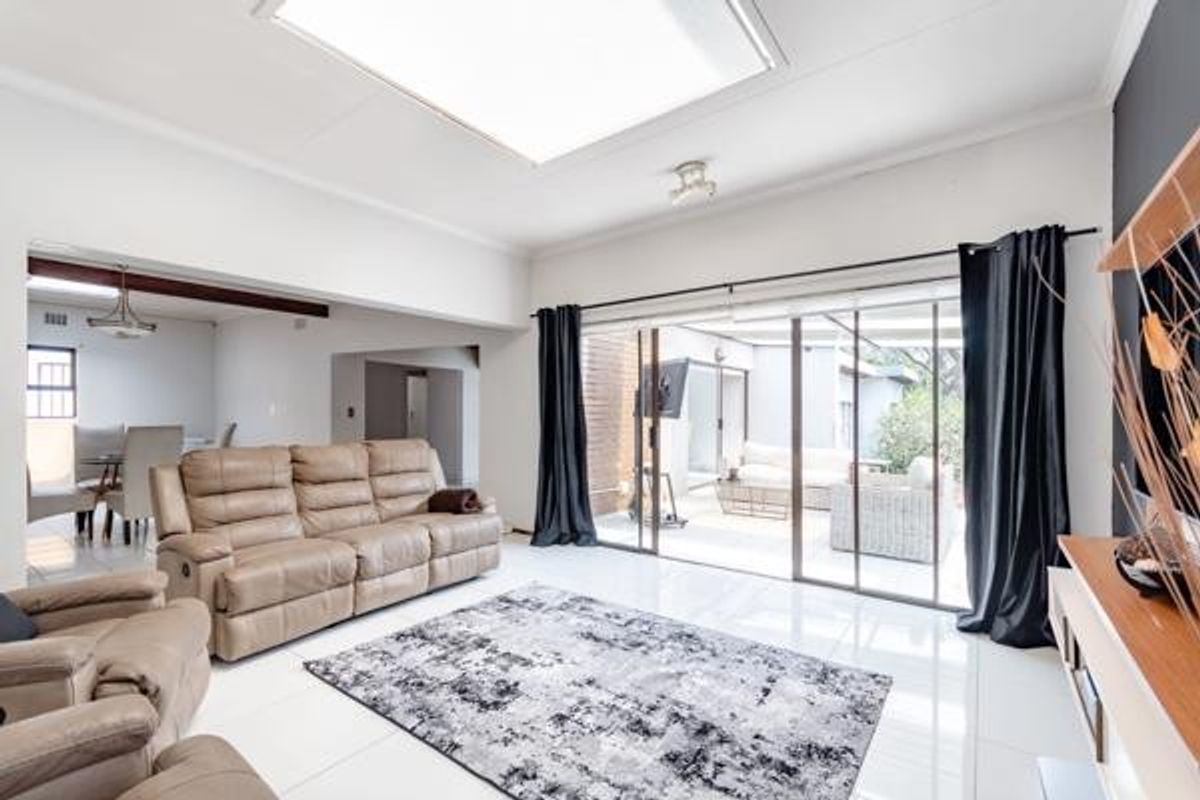 Spacious living room featuring large sliding glass doors leading to an outdoor patio, bright tiled flooring, and a central skylight for natural illumination.