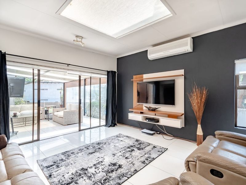 Modern living room featuring tiled floors, a large skylight, split-system air conditioning, and sliding glass doors providing seamless access to the outdoor patio area.