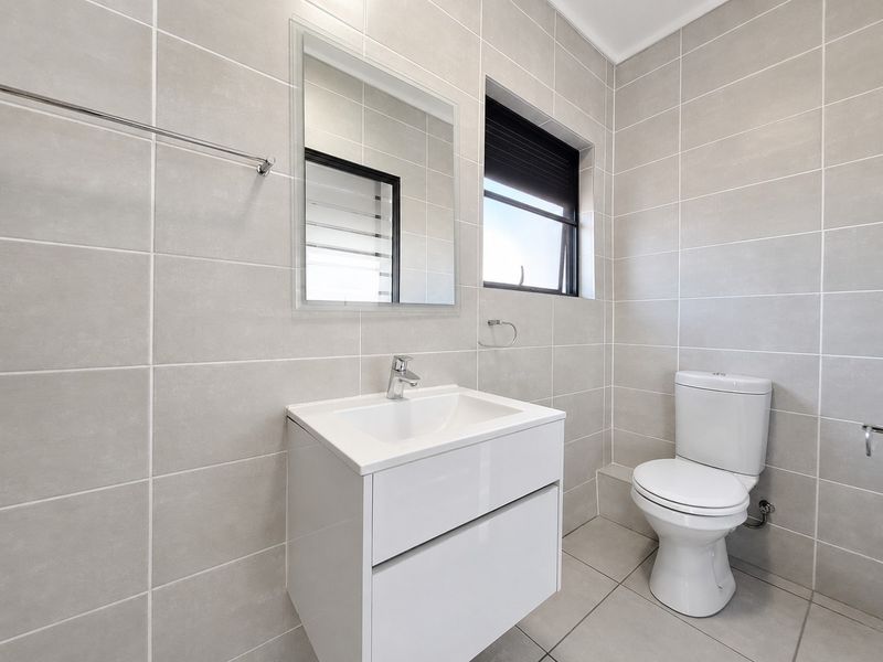 Modern bathroom featuring neutral wall tiles, a sleek wall-mounted vanity with basin, and a clean, contemporary toilet suite.