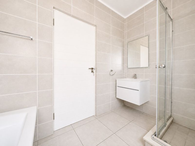 Modern bathroom featuring neutral wall and floor tiles, a wall-mounted vanity, and a glass-enclosed shower.