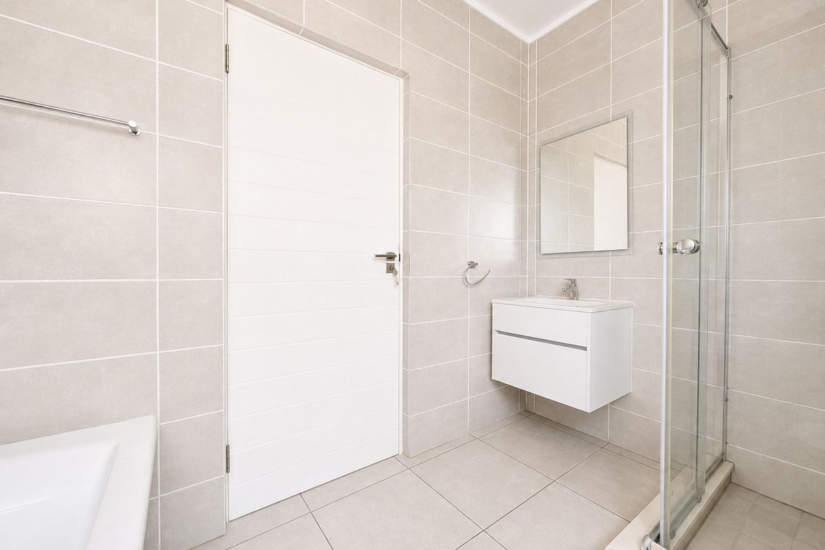 Modern bathroom featuring neutral wall and floor tiles, a wall-mounted vanity, and a glass-enclosed shower.