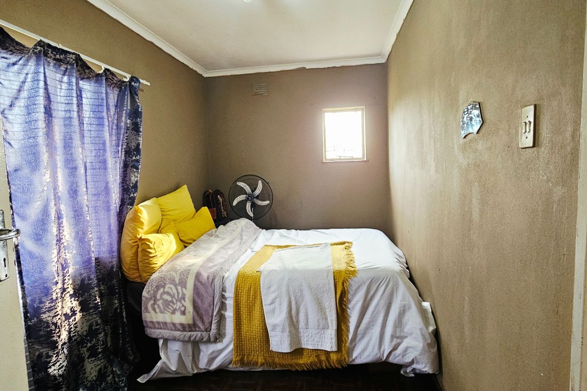 A compact bedroom featuring parquet flooring, coved ceilings, and a small window, providing a functional space with potential for cosmetic updates.