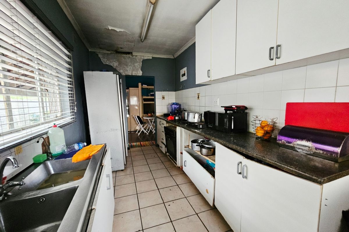 A dated kitchen featuring white cabinetry, tiled flooring, and a double bowl sink, currently requiring significant ceiling repairs and general refurbishment.