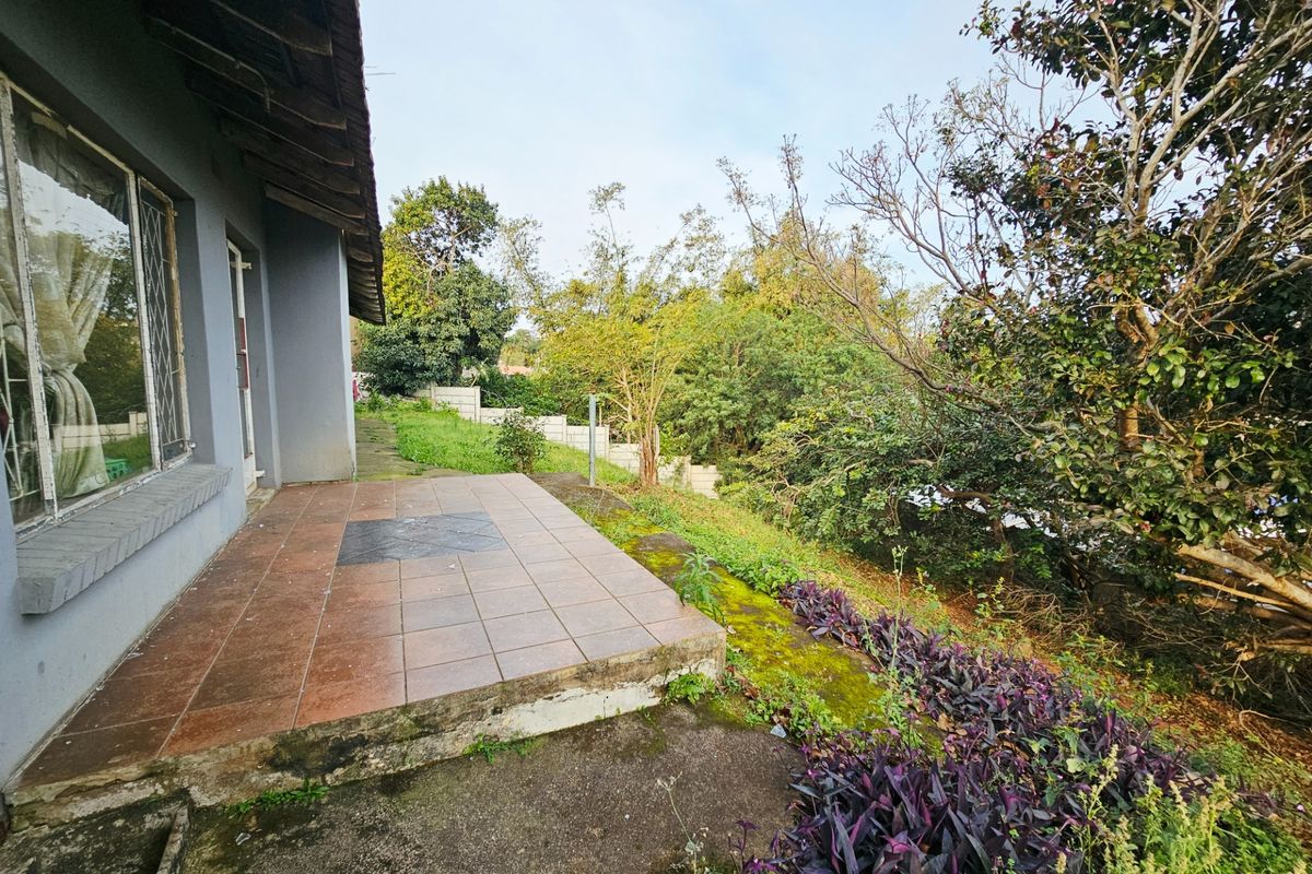 Rear exterior view featuring a tiled patio area, concrete pathways, and a garden with established trees and boundary walling.
