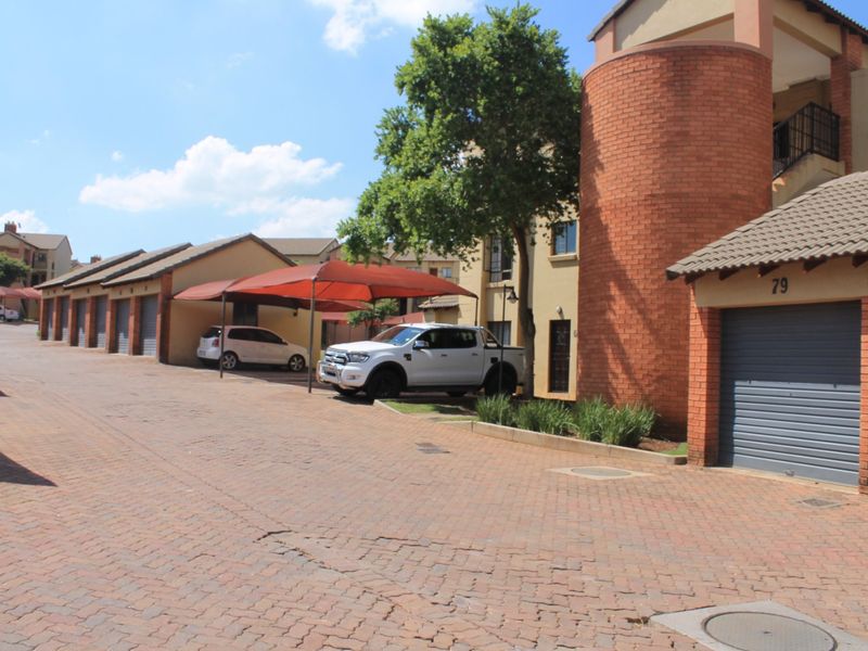 Exterior view of an apartment complex featuring brick paved driveway, individual garage units, and covered parking bays.