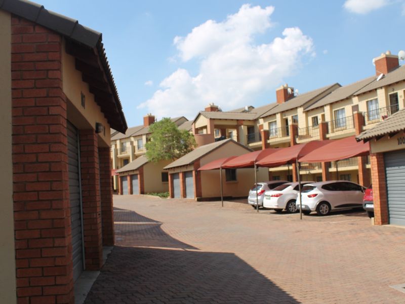 Exterior view of an apartment complex featuring brick facades, tiled roofs, paved driveway, and covered parking bays.