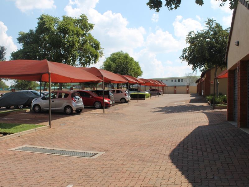 Exterior view of the apartment complex parking area featuring paved driveways, covered shade cloth carports, and brick-finished garage structures.