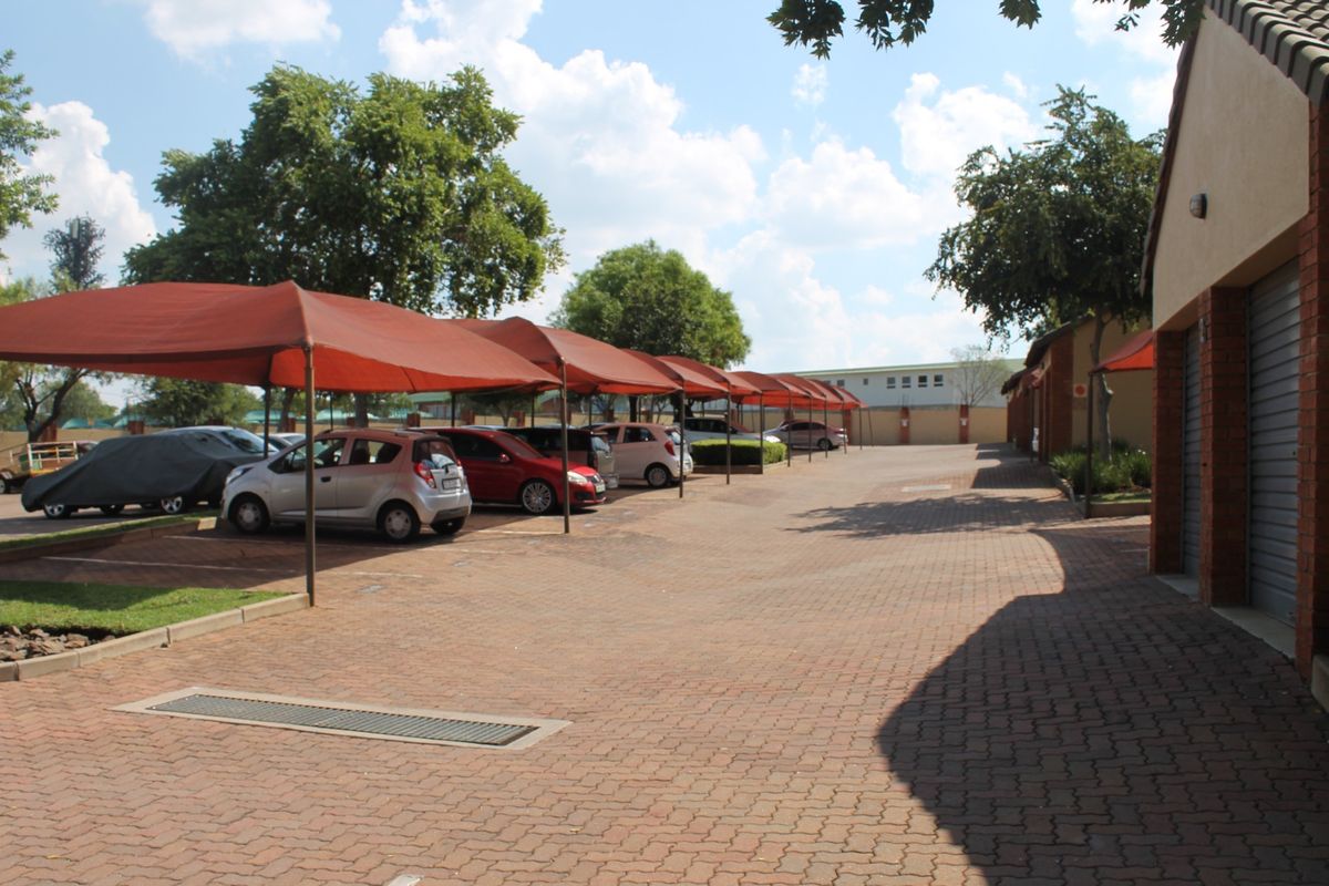 Exterior view of the apartment complex parking area featuring paved driveways, covered shade cloth carports, and brick-finished garage structures.