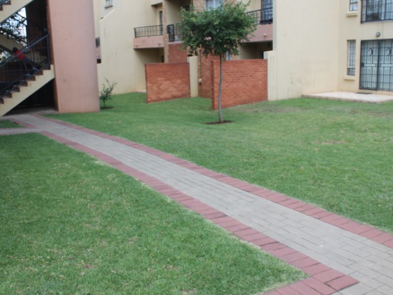 Communal garden area featuring a paved walkway, brick boundary walls, and access to apartment building staircases and entrances.