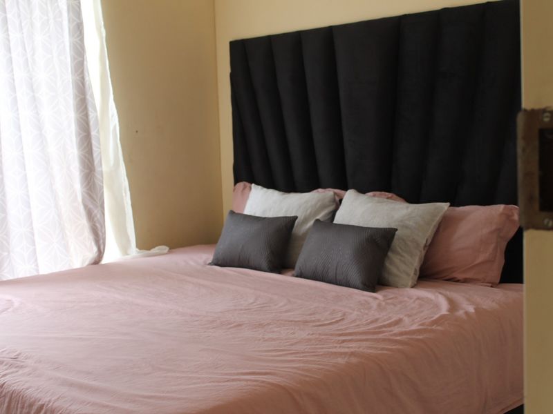 A bedroom interior featuring a large headboard and natural light from the adjacent window.