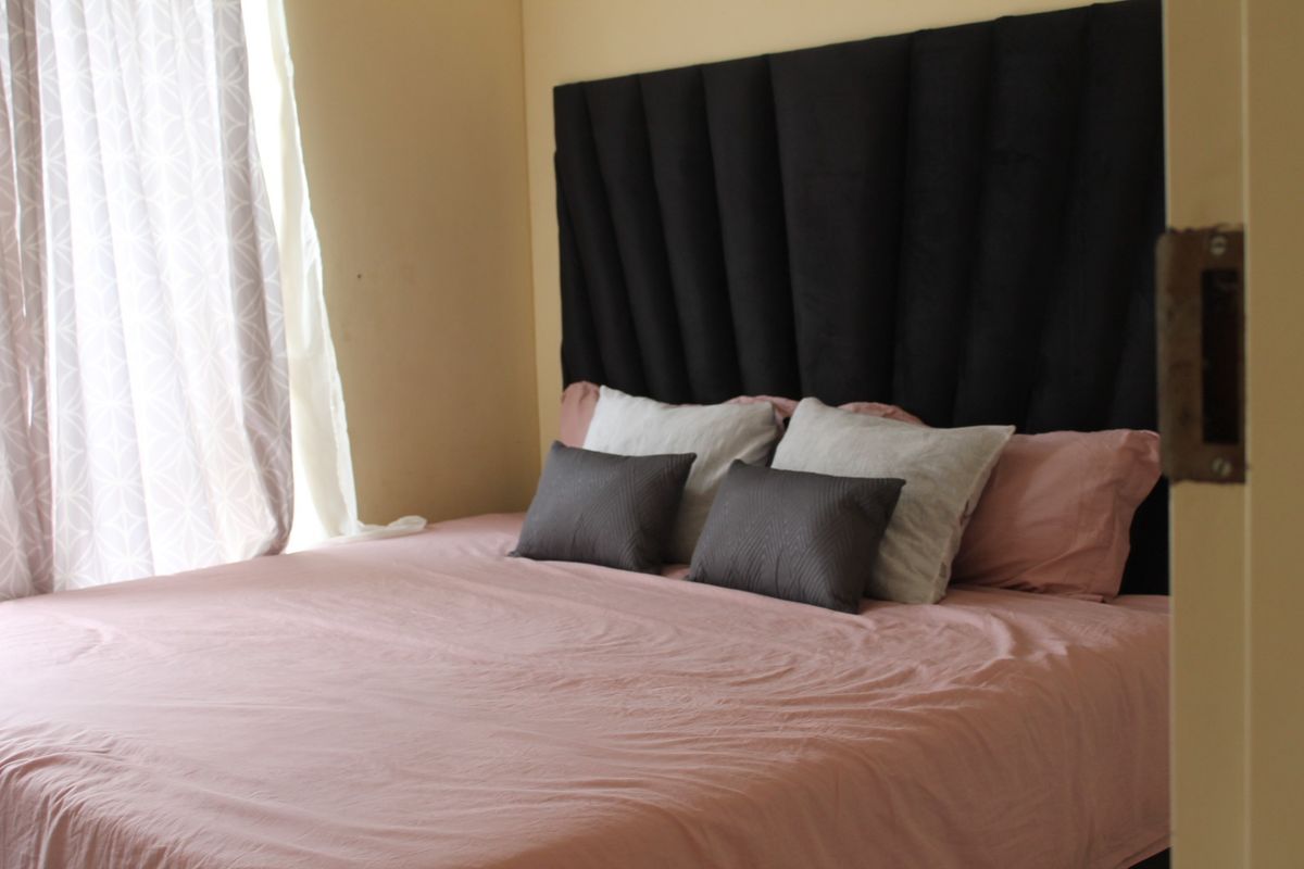 A bedroom interior featuring a large headboard and natural light from the adjacent window.