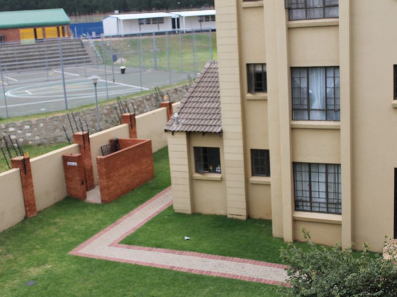 Rear view of the apartment building showing a landscaped garden, paved walkway, and secure boundary wall with electric fencing.