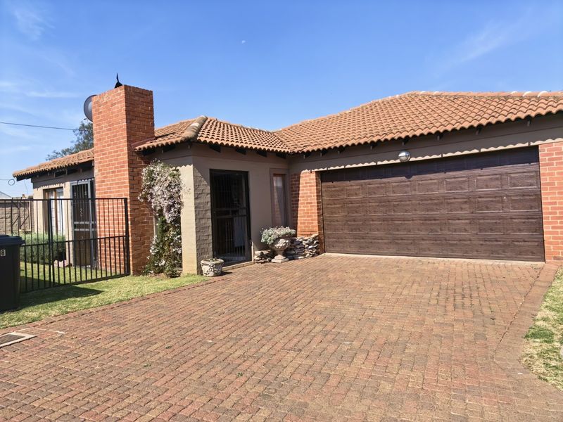 Front elevation of a single-story house featuring a paved driveway, double garage, and brick chimney detail.