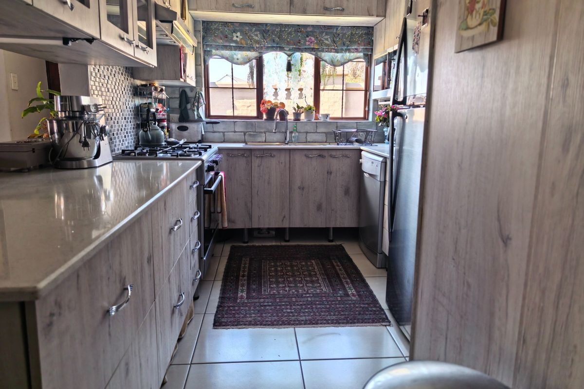 A functional galley-style kitchen featuring wood-look cabinetry, stone countertops, a gas hob, and tiled flooring with ample storage space.