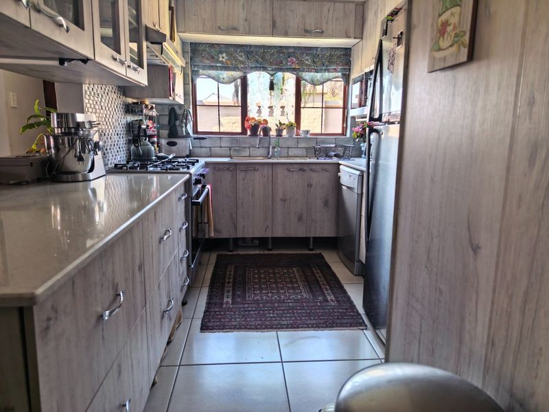 A functional galley-style kitchen featuring wood-look cabinetry, stone countertops, a gas hob, and tiled flooring with ample storage space.
