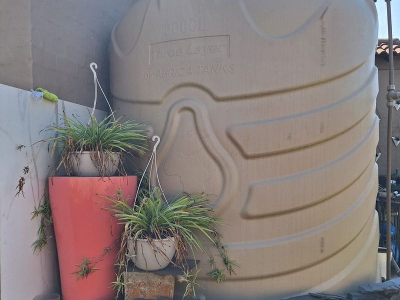 A large 5000L water storage tank installed on a stone-clad base in the rear exterior area of the property.