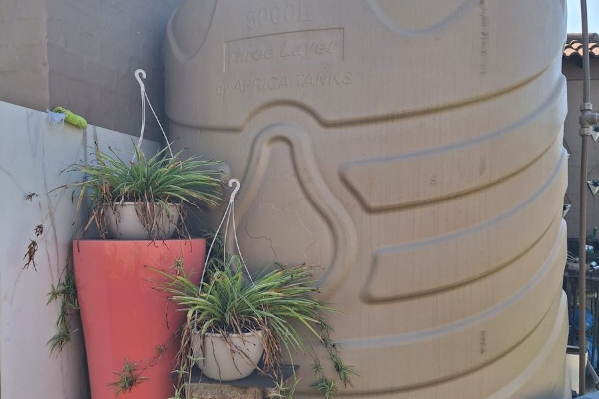 A large 5000L water storage tank installed on a stone-clad base in the rear exterior area of the property.