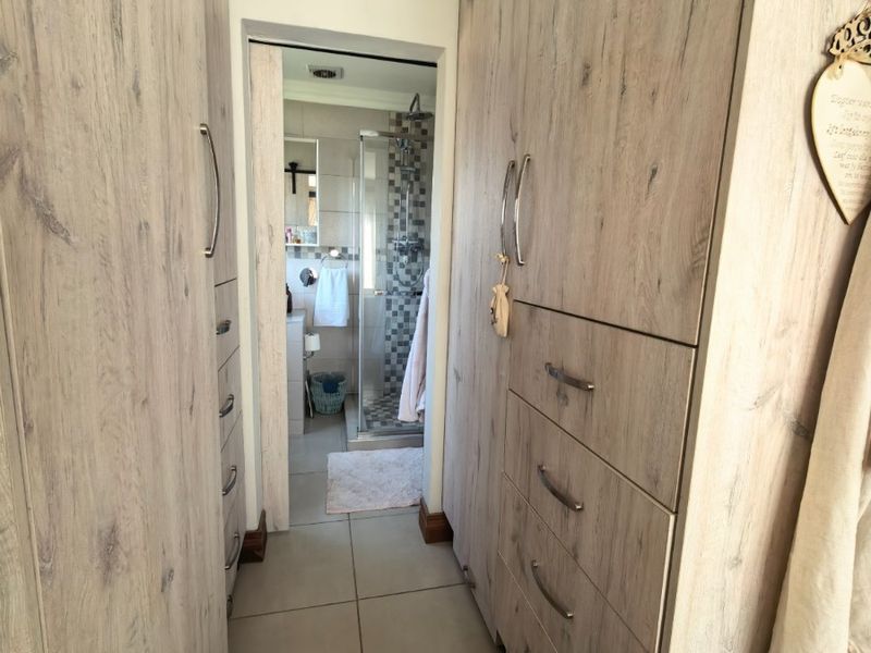 A functional dressing area featuring extensive built-in cabinetry with wood-grain finish, leading directly into a modern tiled bathroom with a glass shower enclosure.