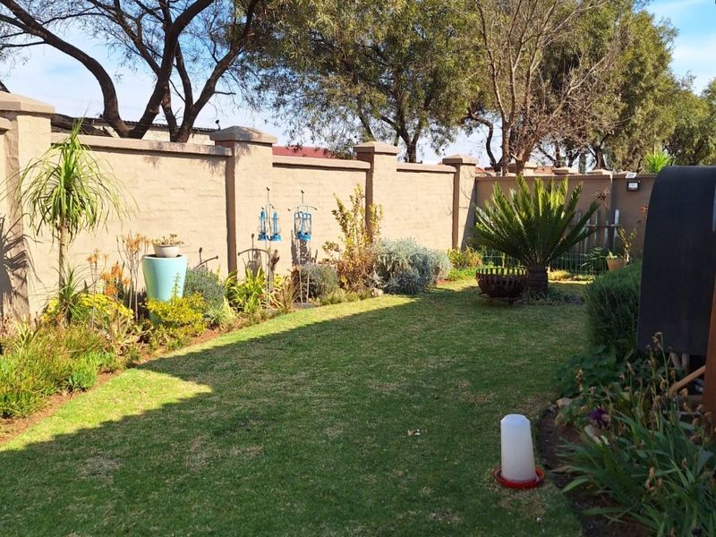 A well-maintained private garden featuring a manicured lawn and a solid perimeter boundary wall with established trees providing privacy.
