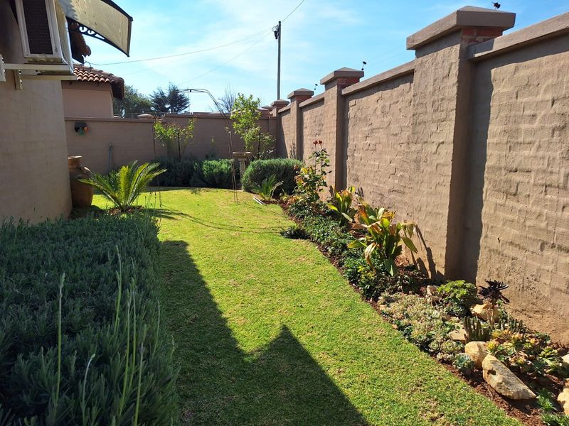 A well-maintained side garden featuring a manicured lawn, established garden beds with succulents and shrubs, enclosed by a solid boundary wall.