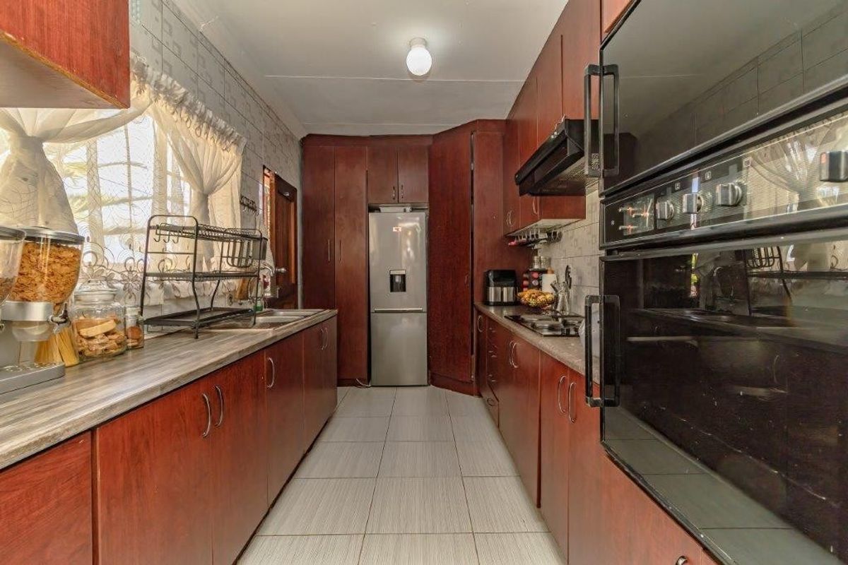 A functional galley-style kitchen featuring dark wood cabinetry, laminate countertops, built-in oven, extractor fan, and tiled flooring.