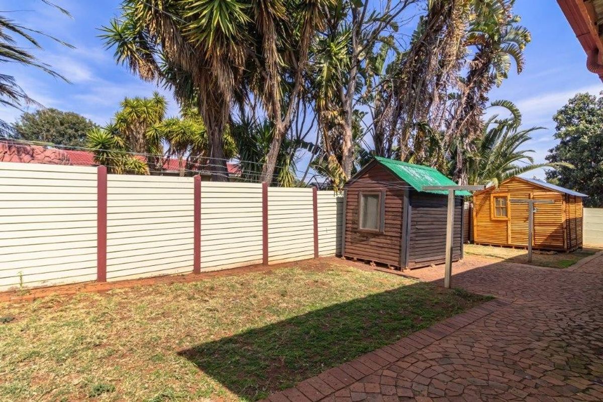 Rear garden area featuring a paved patio, lawn, perimeter wall with electric fencing, and two wooden storage sheds.