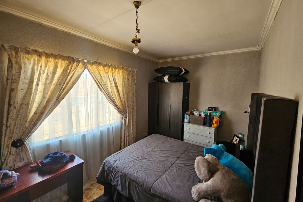 A bedroom featuring a built-in wardrobe, ceiling cornice, and security bars on the window, requiring cosmetic updates to the walls and ceiling.