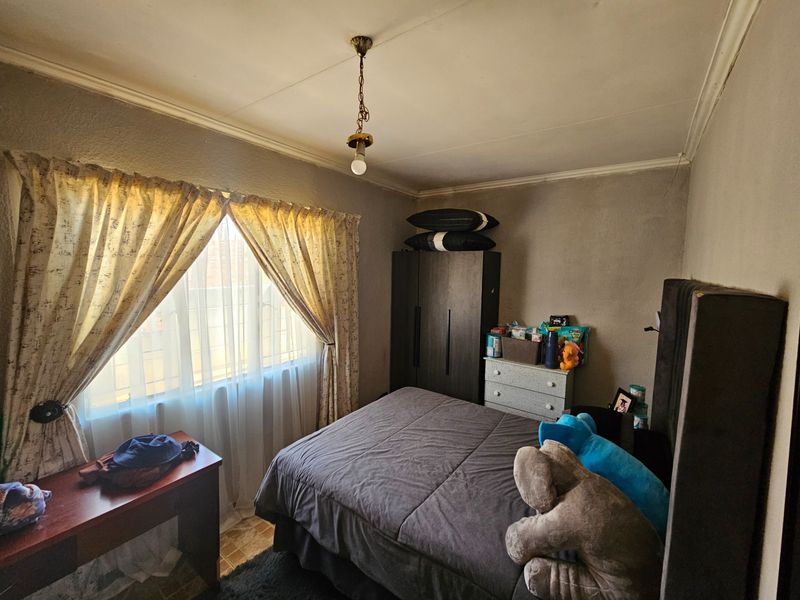 A bedroom featuring a built-in wardrobe, ceiling cornice, and security bars on the window, requiring cosmetic updates to the walls and ceiling.